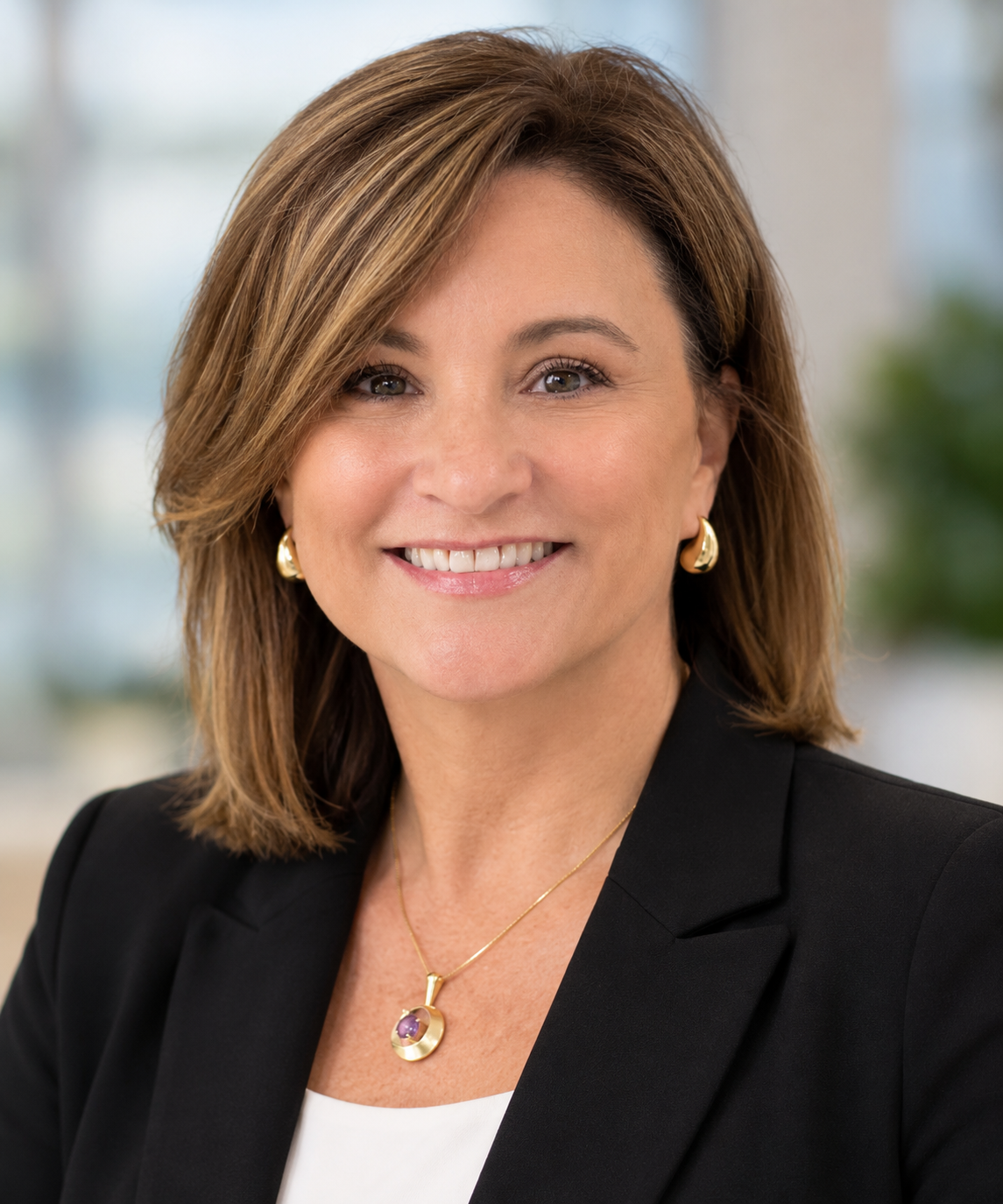 Angela Lang, new clinical director of Milk Bank WGL in a white shirt with a blurred office background and a dark suit jacket smiling at the camera shoulders up portrait